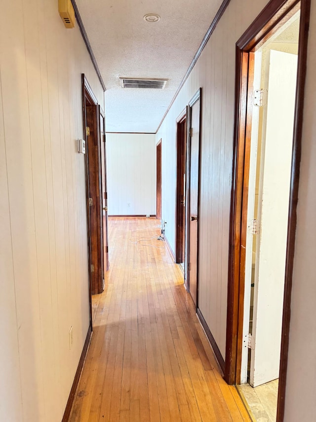 corridor with a textured ceiling, ornamental molding, wooden walls, and light hardwood / wood-style floors