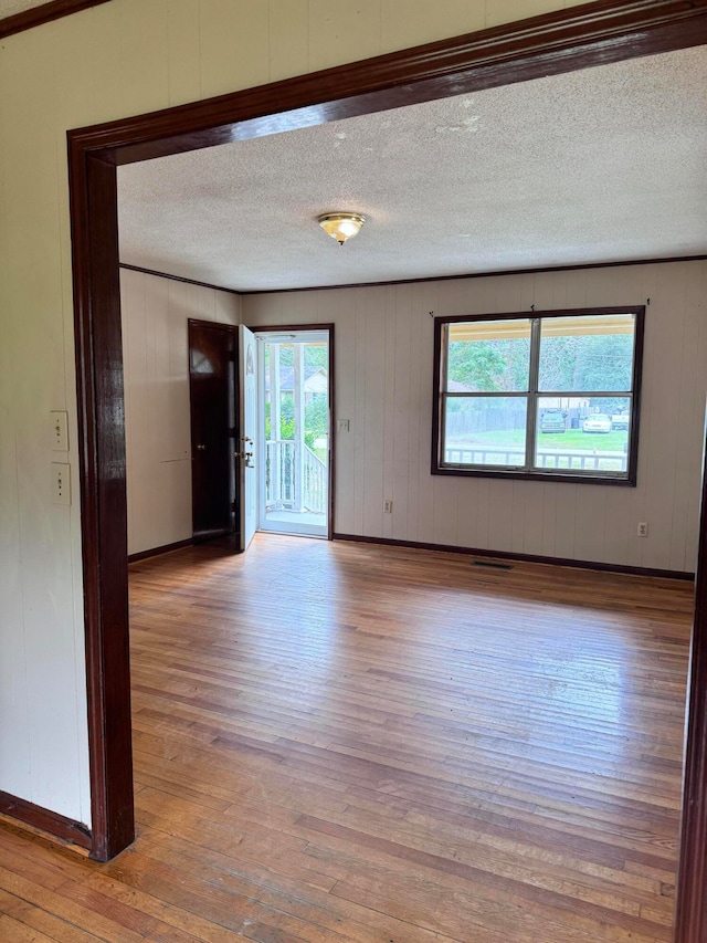 unfurnished room with a textured ceiling, wooden walls, and light hardwood / wood-style floors