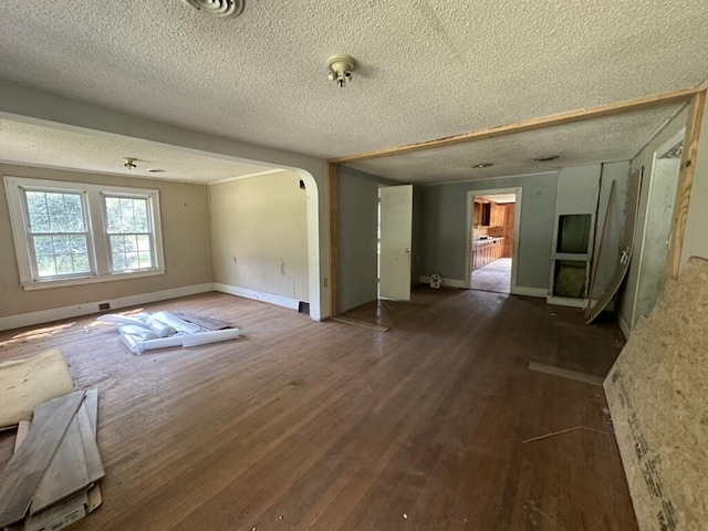 spare room with arched walkways, dark wood finished floors, a textured ceiling, and baseboards