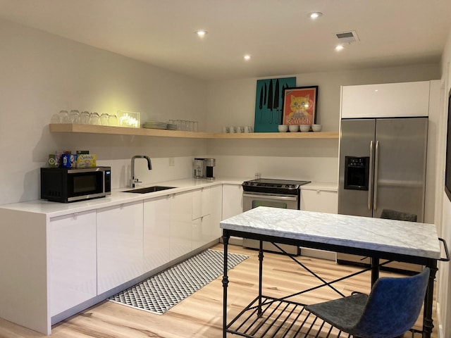 kitchen with appliances with stainless steel finishes, sink, light hardwood / wood-style flooring, and white cabinets