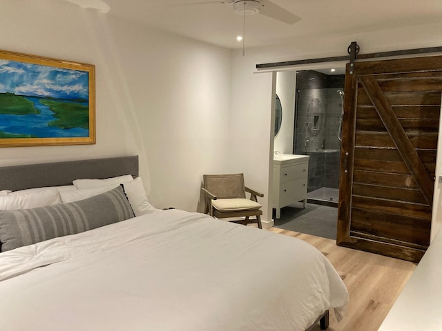 bedroom featuring a barn door, ensuite bath, ceiling fan, and light wood-type flooring