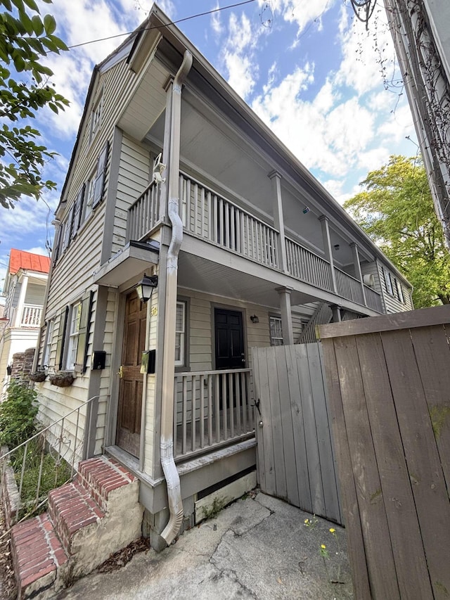 view of property exterior with a porch, a balcony, and fence