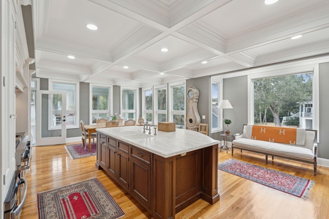 kitchen with beamed ceiling, sink, light stone countertops, and an island with sink