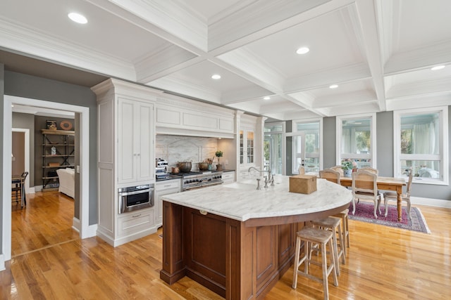 kitchen featuring a breakfast bar, white cabinets, range with two ovens, a kitchen island with sink, and light stone counters