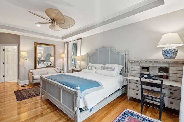 bedroom with hardwood / wood-style flooring, ornamental molding, a raised ceiling, and ceiling fan