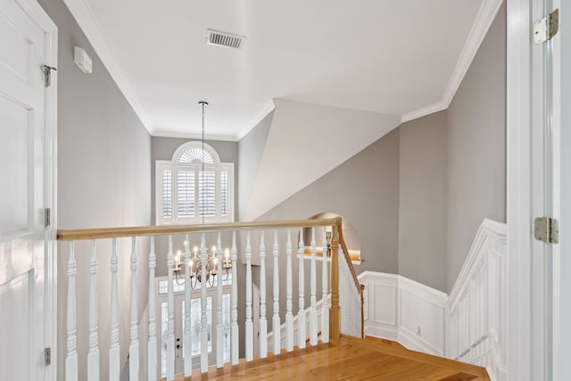 hallway with ornamental molding, wood-type flooring, and an inviting chandelier