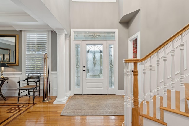 foyer entrance featuring crown molding, decorative columns, and light wood-type flooring