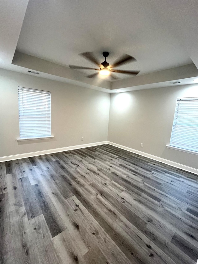 empty room featuring dark hardwood / wood-style floors, ceiling fan, and a tray ceiling