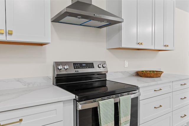 kitchen with wall chimney range hood, white cabinets, light stone counters, and electric stove