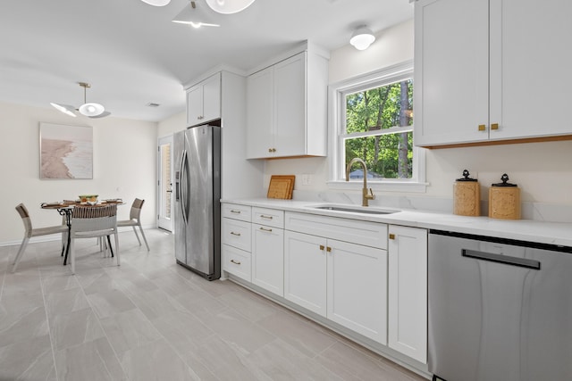 kitchen with appliances with stainless steel finishes, a sink, light countertops, white cabinetry, and pendant lighting