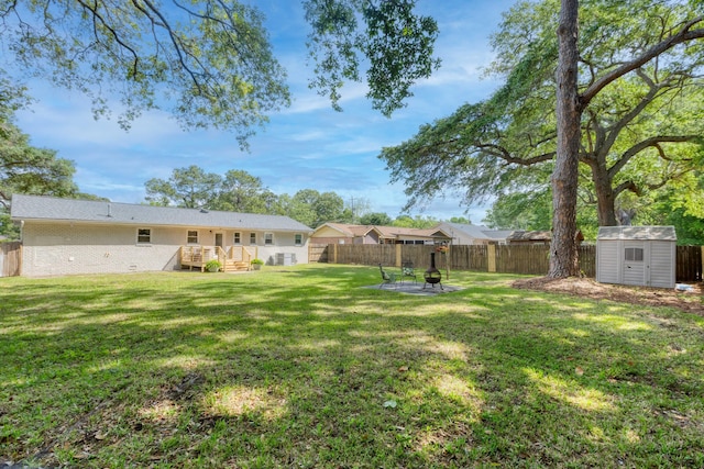 view of yard with a fenced backyard, a storage unit, an outbuilding, and an outdoor fire pit
