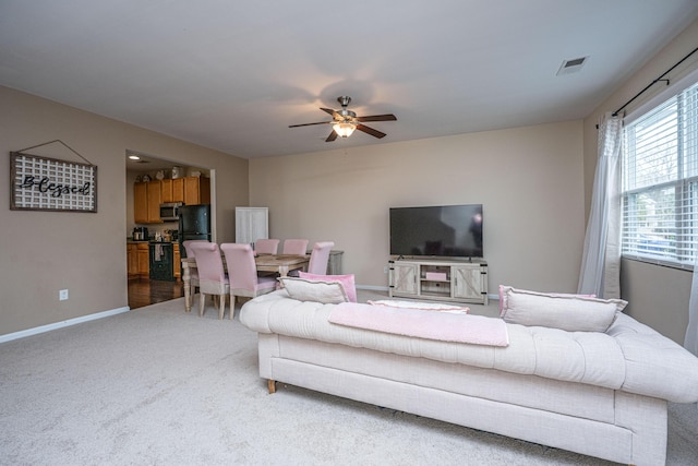 living area featuring light colored carpet, a ceiling fan, visible vents, and baseboards