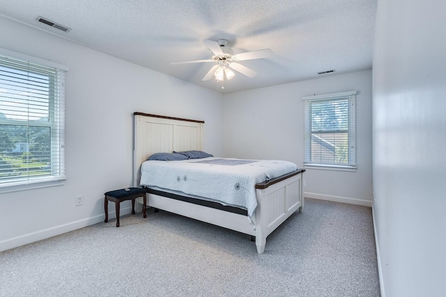 carpeted bedroom featuring ceiling fan, multiple windows, and a textured ceiling