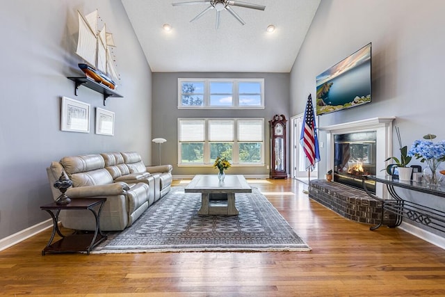 living room with a textured ceiling, high vaulted ceiling, ceiling fan, a fireplace, and light hardwood / wood-style flooring