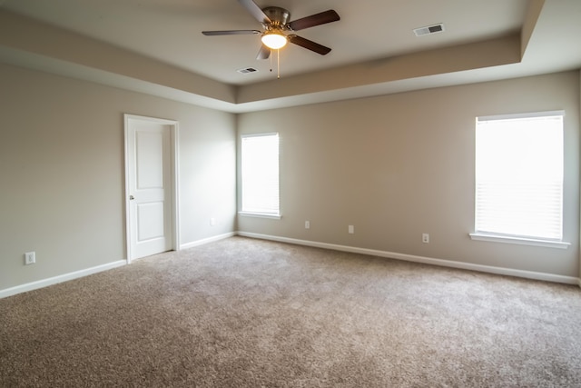 carpeted empty room featuring ceiling fan, baseboards, and a raised ceiling