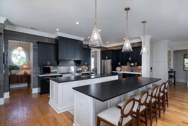 kitchen with a sink, light wood-type flooring, freestanding refrigerator, visible vents, and an island with sink