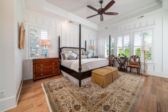 bedroom featuring light wood-style flooring, a decorative wall, ornamental molding, and visible vents