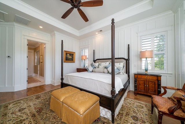bedroom with visible vents, wood finished floors, ornamental molding, and a decorative wall