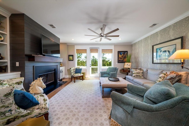 living room with visible vents, a fireplace with raised hearth, ceiling fan, and crown molding