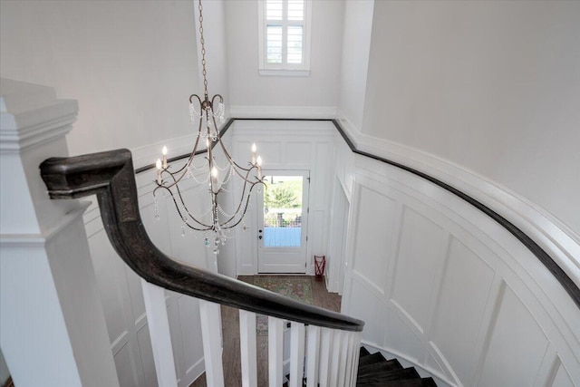 stairs with a decorative wall, wainscoting, a healthy amount of sunlight, and an inviting chandelier