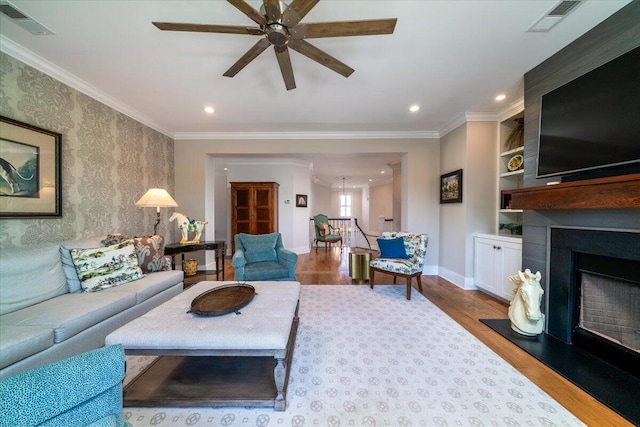 living room with recessed lighting, a fireplace with raised hearth, a ceiling fan, wood finished floors, and ornamental molding