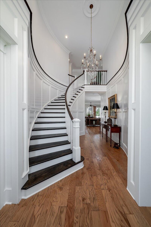 stairs with wood finished floors, a high ceiling, crown molding, and a notable chandelier