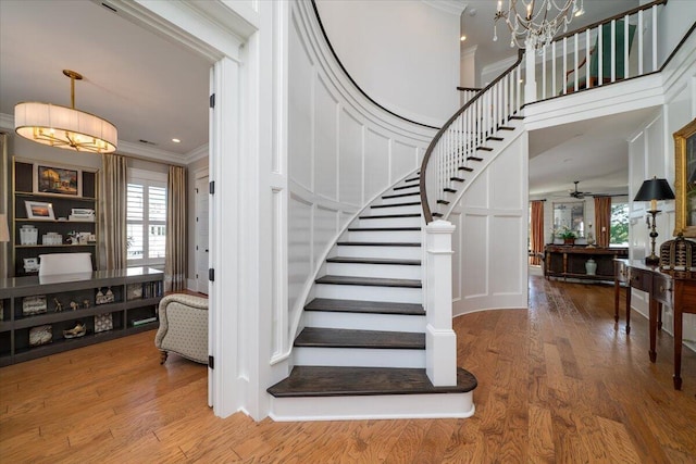 stairway featuring a wealth of natural light, crown molding, wood finished floors, and an inviting chandelier