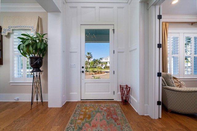 foyer with plenty of natural light, baseboards, wood finished floors, and ornamental molding