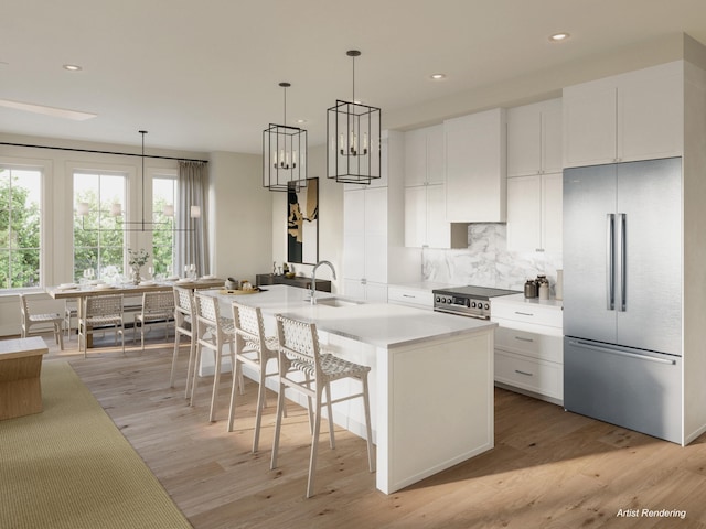 kitchen with white cabinetry, premium appliances, light hardwood / wood-style flooring, and an island with sink