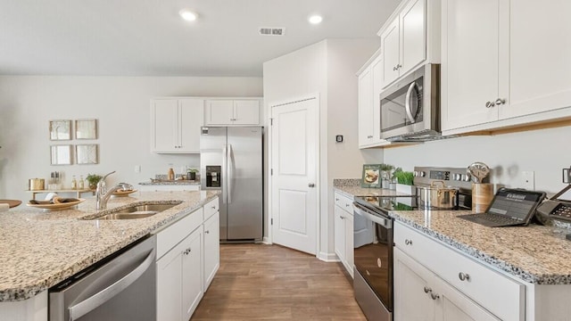 kitchen with stainless steel appliances, a sink, wood finished floors, white cabinets, and recessed lighting