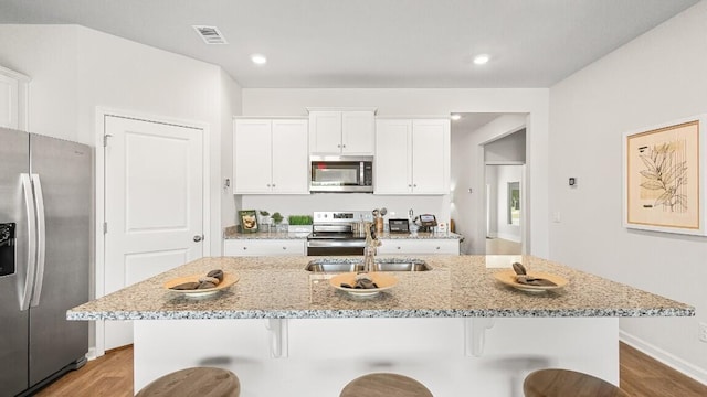 kitchen with stainless steel appliances, a kitchen breakfast bar, light wood-style flooring, a sink, and white cabinets