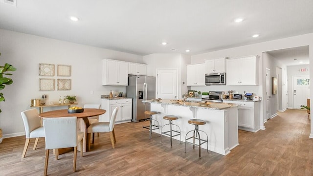 kitchen featuring appliances with stainless steel finishes, an island with sink, white cabinetry, wood finished floors, and a breakfast bar area
