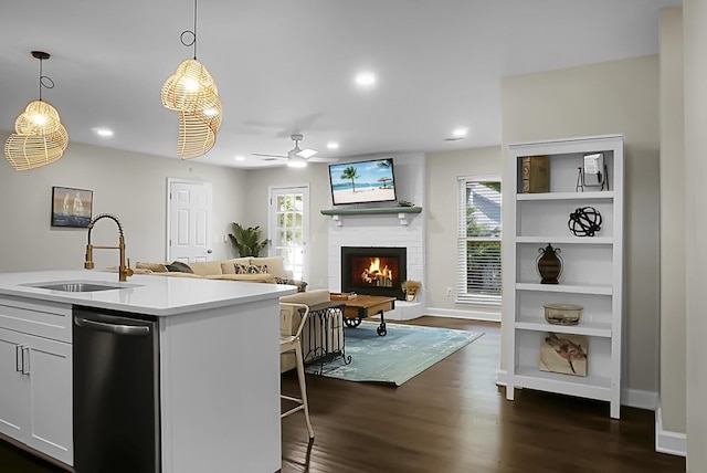 kitchen featuring decorative light fixtures, light countertops, stainless steel dishwasher, a sink, and a warm lit fireplace