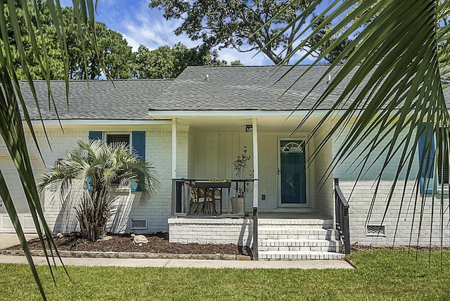 entrance to property with roof with shingles, crawl space, a yard, a porch, and brick siding