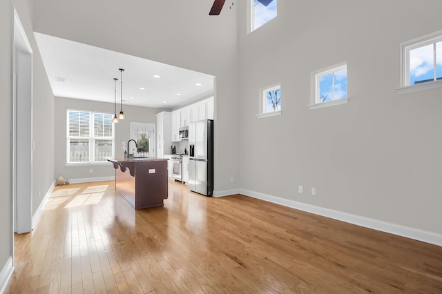 kitchen with pendant lighting, a kitchen island with sink, white cabinets, light wood-type flooring, and stainless steel appliances