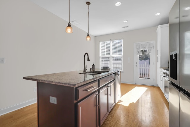 kitchen with pendant lighting, sink, an island with sink, dark brown cabinets, and light hardwood / wood-style floors