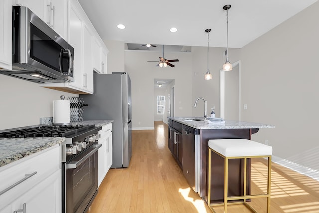 kitchen with ceiling fan, a kitchen breakfast bar, an island with sink, white cabinets, and appliances with stainless steel finishes