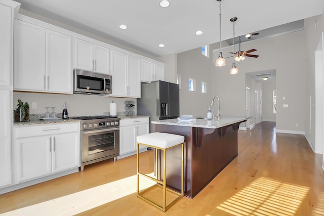 kitchen with a kitchen bar, stainless steel appliances, white cabinetry, and an island with sink