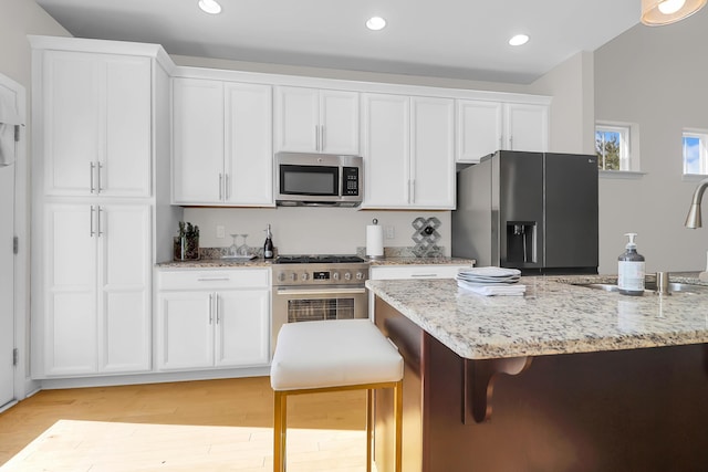 kitchen with white cabinets, light hardwood / wood-style flooring, appliances with stainless steel finishes, light stone counters, and a breakfast bar area