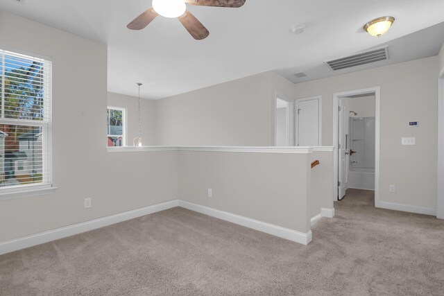 empty room featuring ceiling fan, light colored carpet, and a healthy amount of sunlight