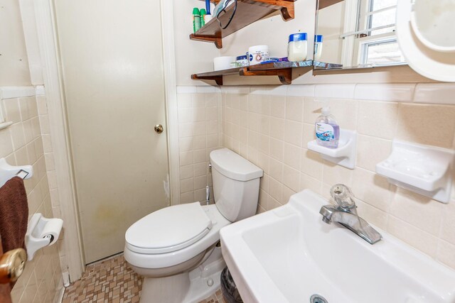 bathroom with toilet, sink, and tile walls