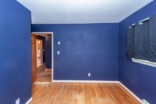 spare room featuring hardwood / wood-style floors, a textured ceiling, and a baseboard heating unit