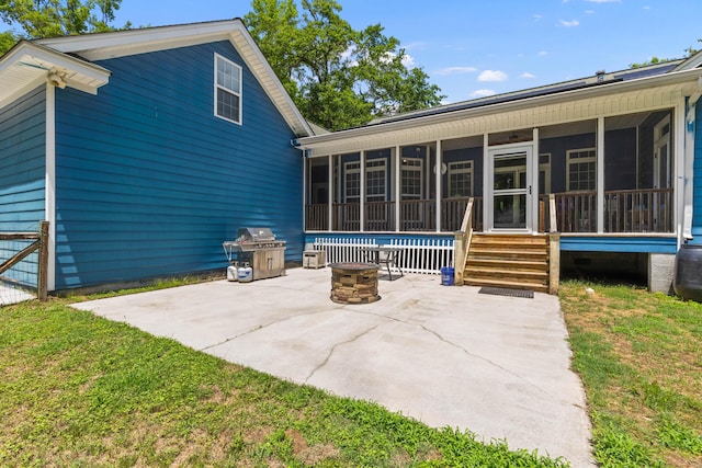 back of house featuring a sunroom, a patio area, a fire pit, and a lawn