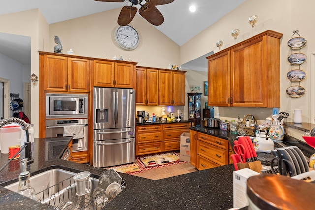 kitchen featuring stainless steel appliances, ceiling fan, brown cabinetry, high vaulted ceiling, and dark stone counters