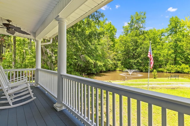 wooden deck with a lawn, a water view, ceiling fan, and view of wooded area