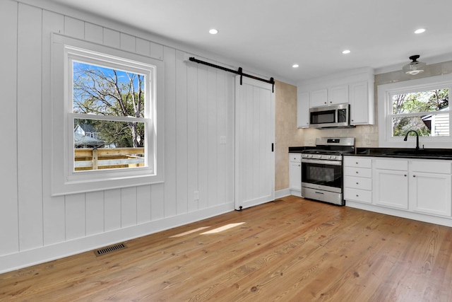 kitchen with white cabinetry, sink, a barn door, appliances with stainless steel finishes, and light hardwood / wood-style flooring