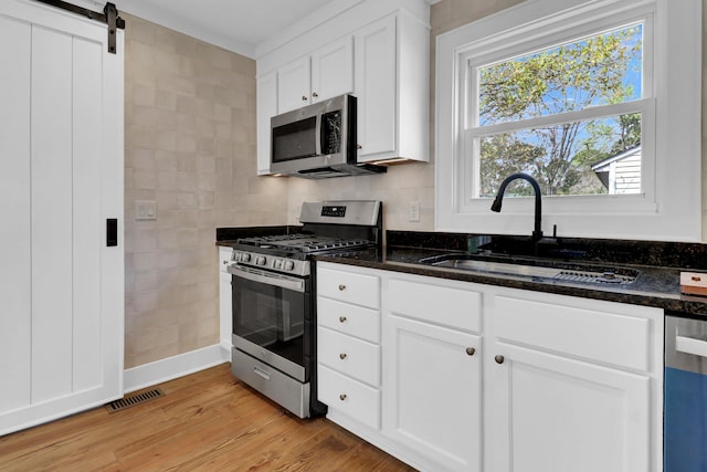 kitchen featuring dark stone countertops, light wood-type flooring, a barn door, stainless steel appliances, and sink