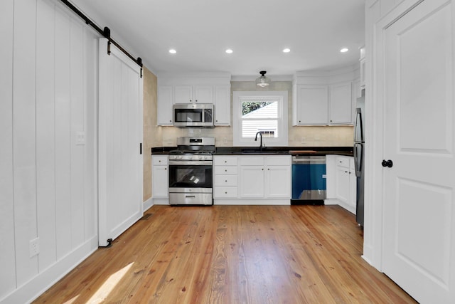 kitchen featuring a barn door, white cabinets, light wood-type flooring, and stainless steel appliances