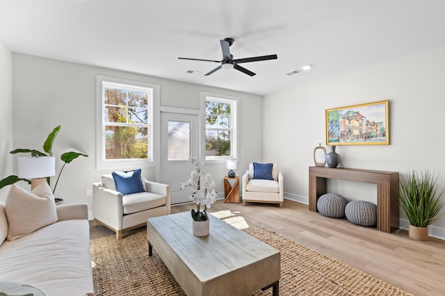 living room with light wood-type flooring, visible vents, ceiling fan, and baseboards