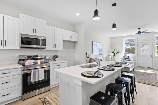 kitchen featuring appliances with stainless steel finishes, a kitchen island with sink, light countertops, white cabinetry, and a sink